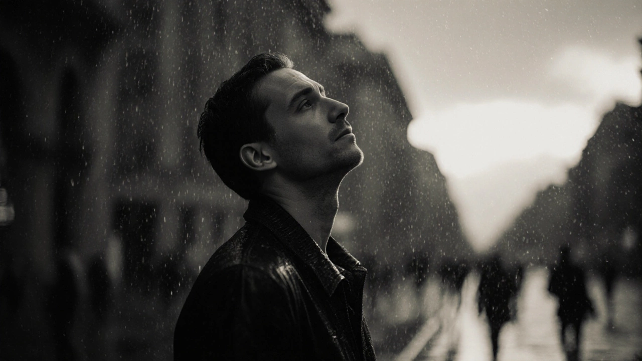 Мужчина смотрит на небо под легким дождём, прохожие не замечают его — тишина и одиночество.